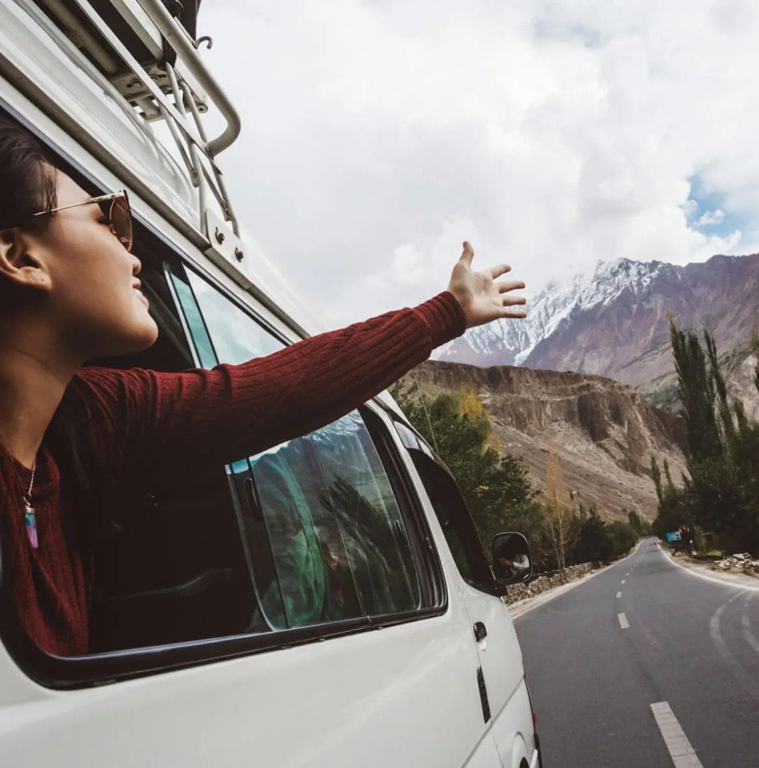 Woman in van with arm out the window while driving in the mountains
